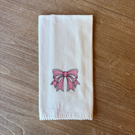 White towel with an embroidered pink bow design on a wooden surface