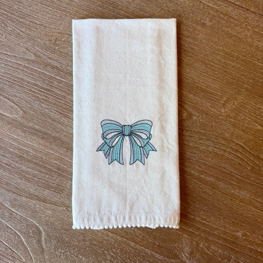 White towel with a blue bow design embroidered on a wooden surface